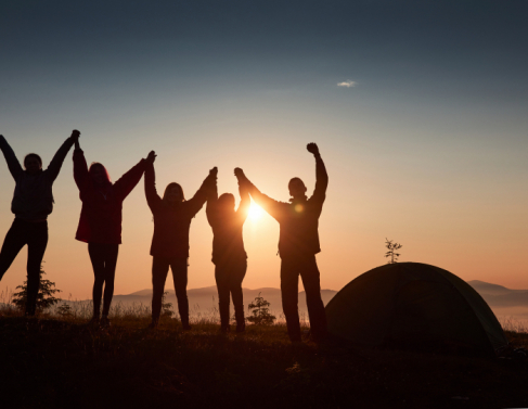 A silhouette of group people have fun at the top of the mountain near the tent during the sunset.