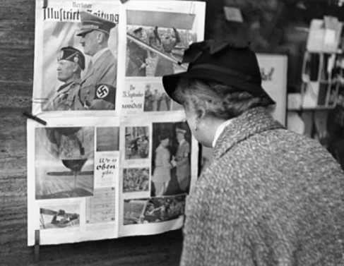 Senhora alemã lendo propaganda nazista exposta em locais públicos. 